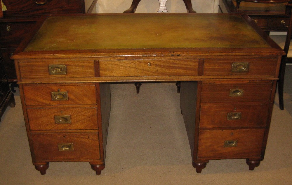 Solid mahogany military campaign pedestal desk featuring an inset leather writing top, flush brass handles, and nine drawers resting on turned feet.