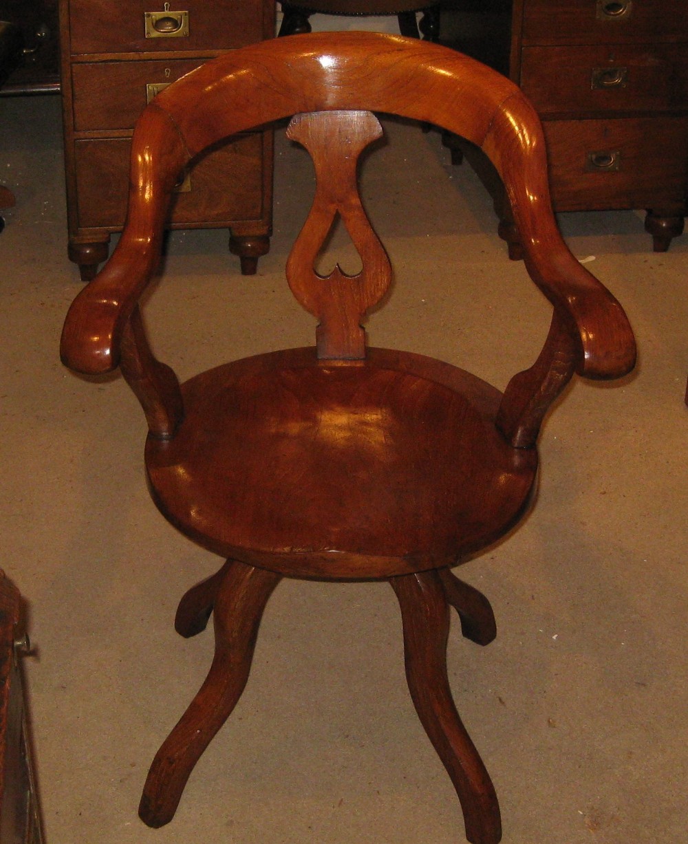 A Victorian walnut revolving desk chair featuring a continuous curved backrail, pierced vase splat, shaped saddle seat, and splayed legs.
