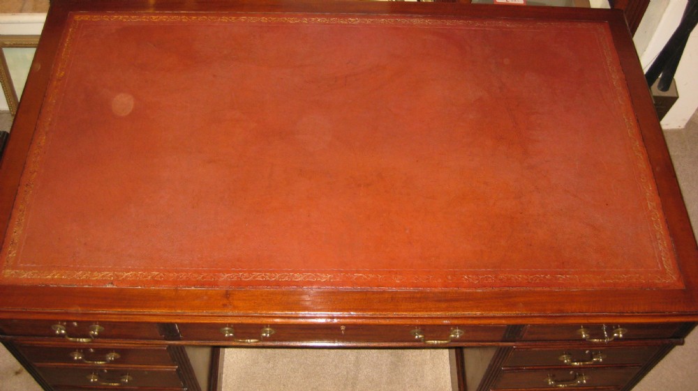 An antique mahogany pedestal desk featuring nine drawers with brass handles and a reddish-brown leather writing surface. View III