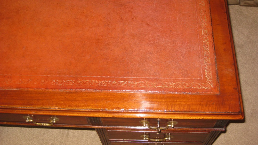 An antique mahogany pedestal desk featuring nine drawers with brass handles and a reddish-brown leather writing surface. View IV