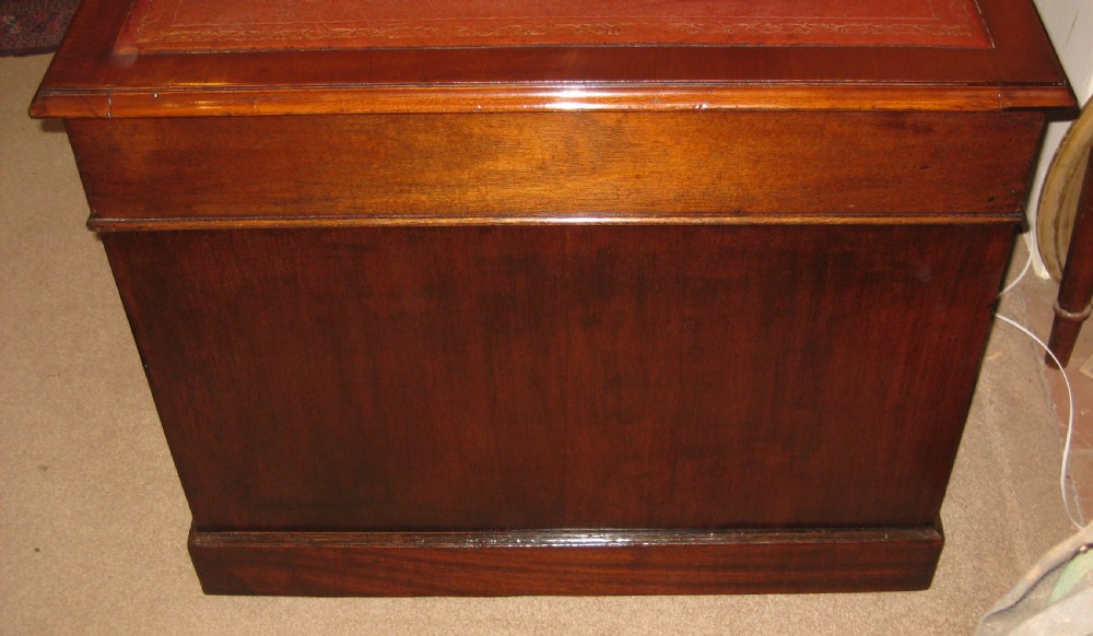 An antique mahogany pedestal desk featuring nine drawers with brass handles and a reddish-brown leather writing surface. View V