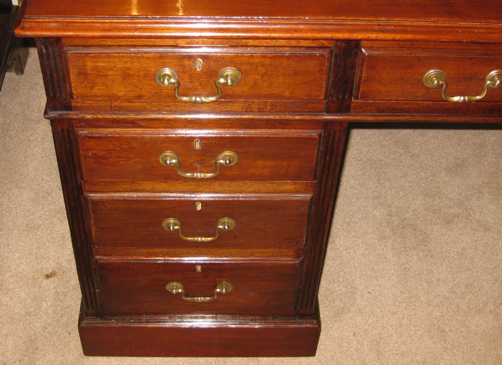 An antique mahogany pedestal desk featuring nine drawers with brass handles and a reddish-brown leather writing surface. View VII