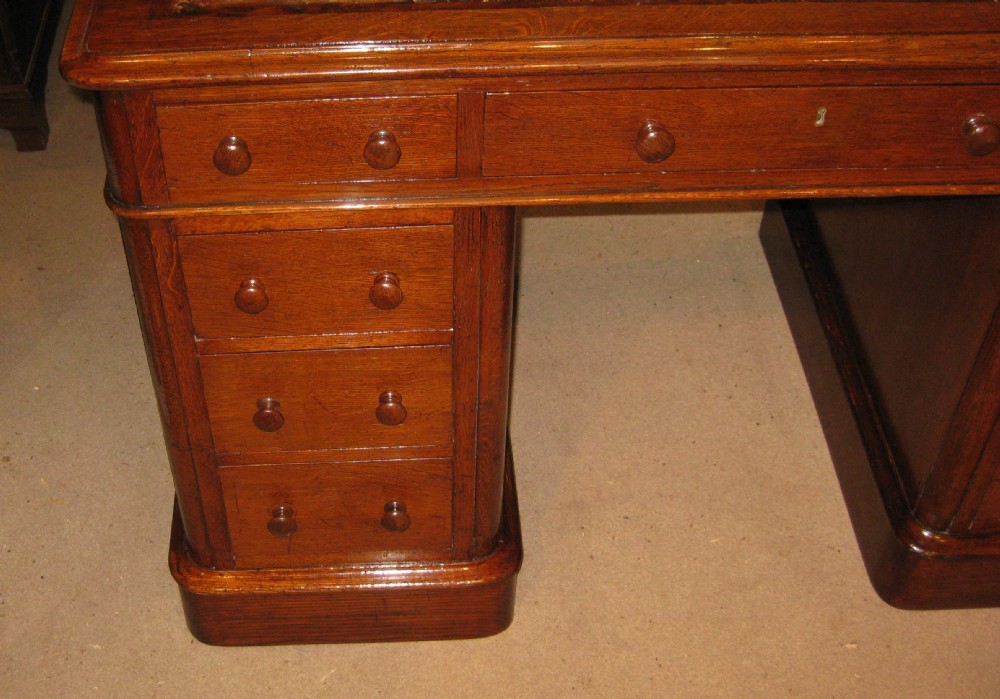 A Victorian oak pedestal desk featuring a leather-inlaid writing top, nine drawers with turned wooden knobs, and double plinth bases. View IV