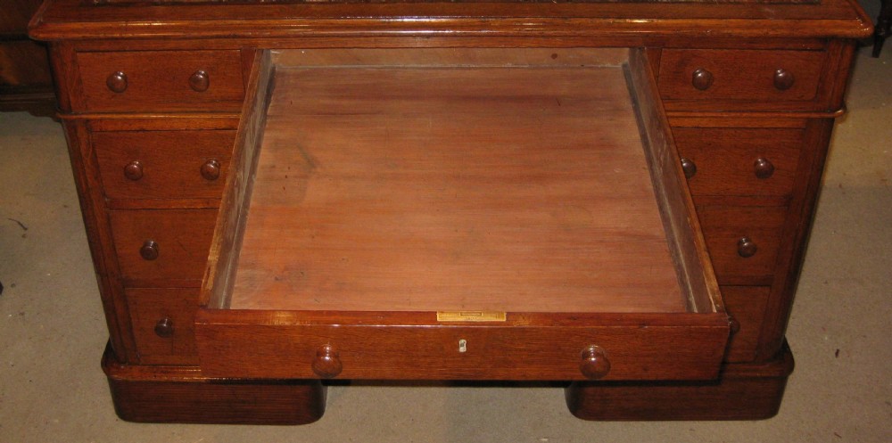 A Victorian oak pedestal desk featuring a leather-inlaid writing top, nine drawers with turned wooden knobs, and double plinth bases. View VI