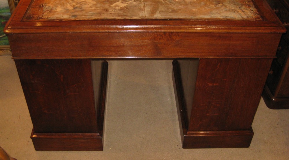 A Victorian oak pedestal desk featuring a leather-inlaid writing top, nine drawers with turned wooden knobs, and double plinth bases. View VII