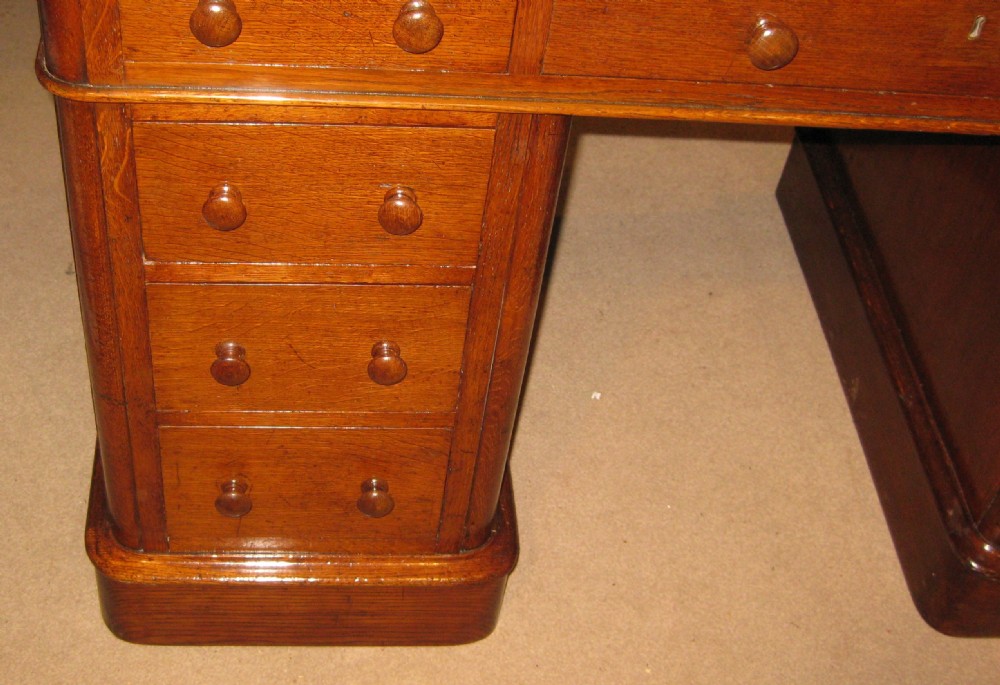 A Victorian oak pedestal desk featuring a leather-inlaid writing top, nine drawers with turned wooden knobs, and double plinth bases. View X