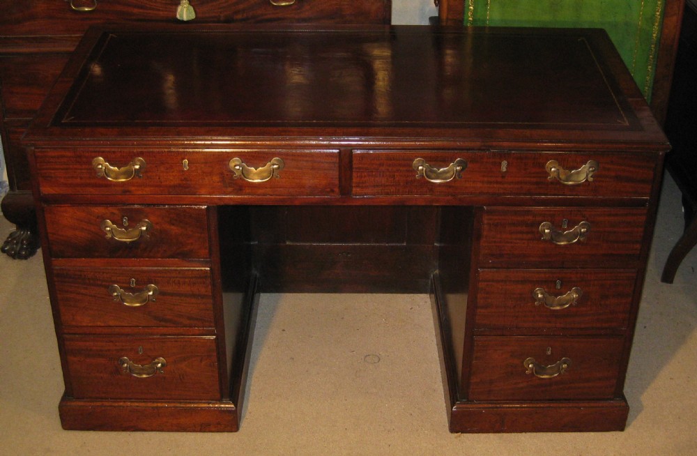 An 18th-century Georgian mahogany kneehole desk featuring a leather inset top, brass swan-neck handles, and flanking columns of drawers.
