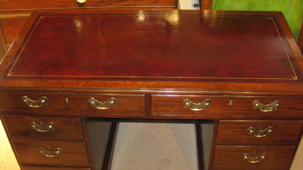 An 18th-century Georgian mahogany kneehole desk featuring a leather inset top, brass swan-neck handles, and flanking columns of drawers. View V