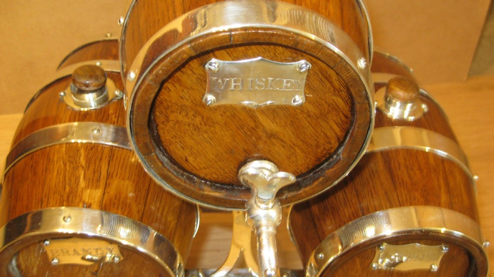 A triple miniature oak spirit barrel dispenser set mounted on a wooden frame with silver-plated hoops, spigots, and metal spirit labels. View III