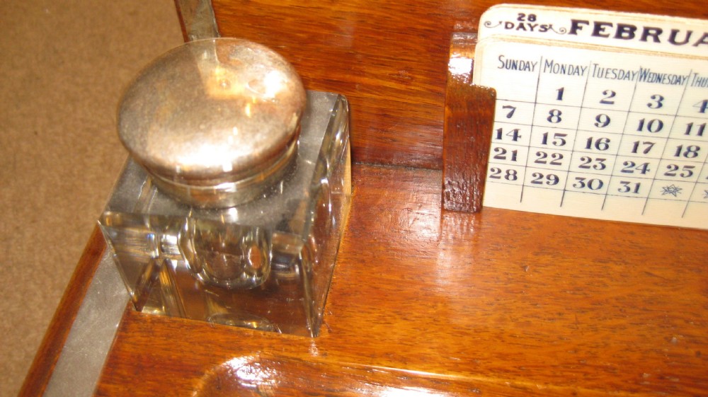 An antique warm brown oak desk inkstand featuring a domed upper stationery compartment with ornate silver-toned metal strapwork, two square glass inkwells, and a lower drawer. View IV