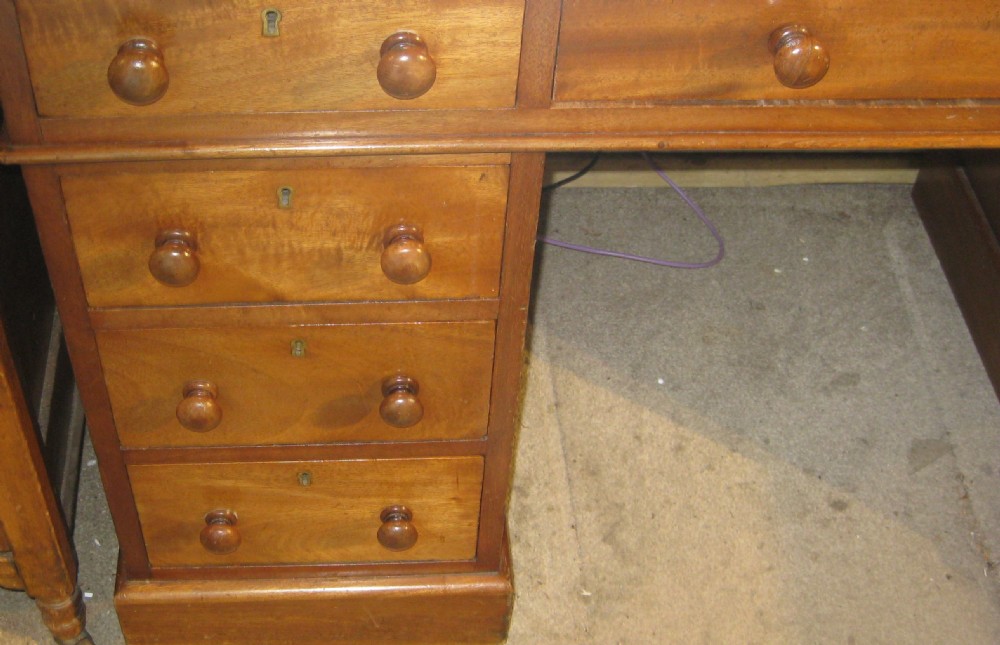 A Victorian golden mahogany pedestal desk featuring an inset green leather writing surface, nine drawers with turned wooden knobs, and a central kneehole. View III