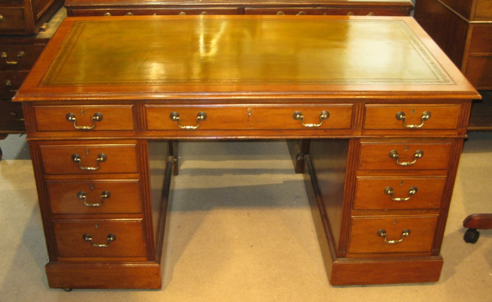 A Victorian golden mahogany pedestal desk featuring an inset green leather writing surface, nine drawers with turned wooden knobs, and a central kneehole. View V