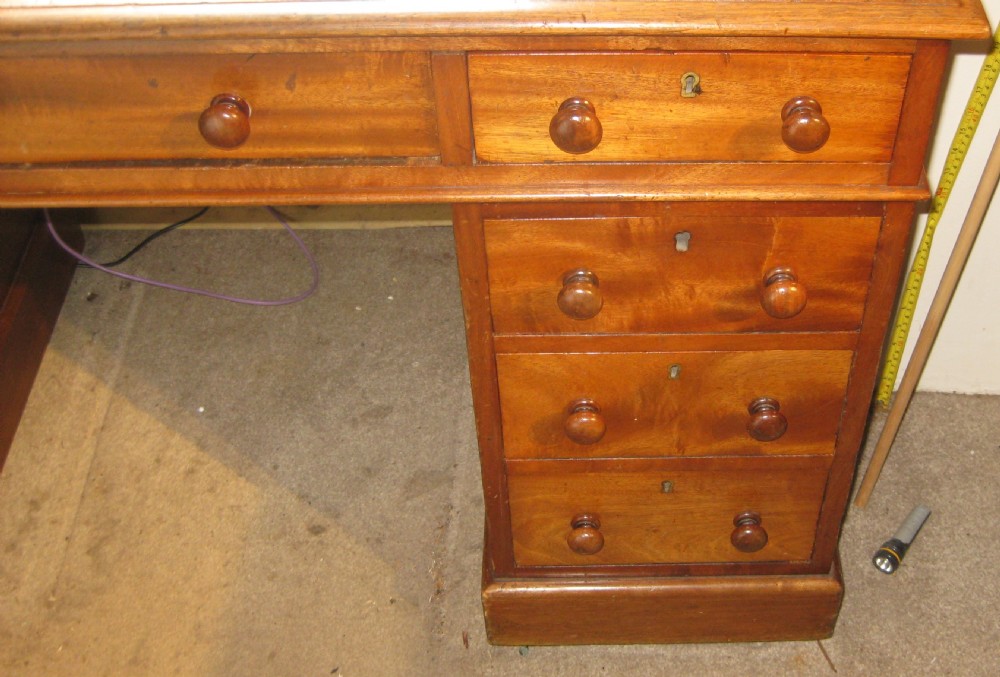 A Victorian golden mahogany pedestal desk featuring an inset green leather writing surface, nine drawers with turned wooden knobs, and a central kneehole. View VI
