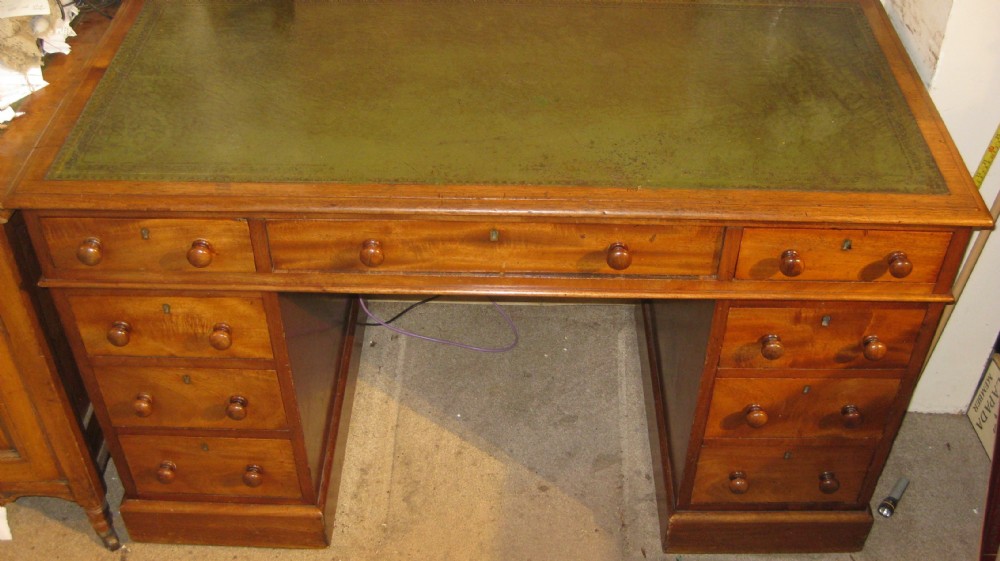 A Victorian golden mahogany pedestal desk featuring an inset green leather writing surface, nine drawers with turned wooden knobs, and a central kneehole.