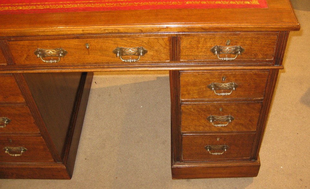 Victorian walnut pedestal desk featuring a red leather gilt-tooled inset writing surface and nine brass-handled drawers. View III