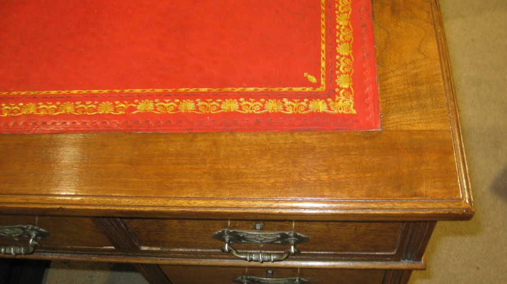 Victorian walnut pedestal desk featuring a red leather gilt-tooled inset writing surface and nine brass-handled drawers. View VI
