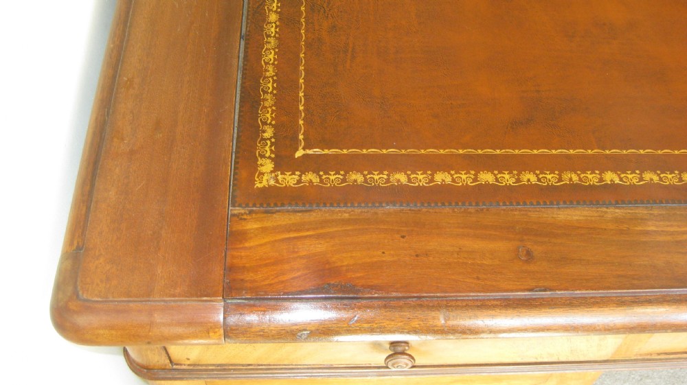 A Victorian faded mahogany pedestal desk featuring a gilt-bordered leather writing surface, three frieze drawers, and twin pedestal cupboards with arched flame mahogany panels. View V