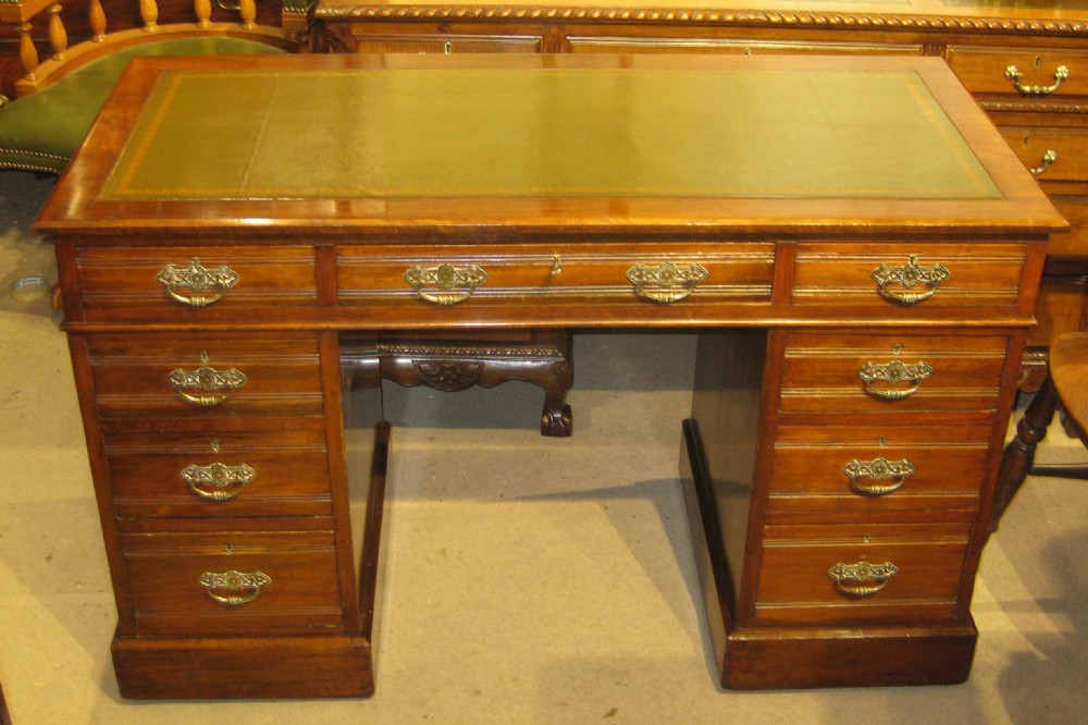 A Victorian walnut pedestal desk featuring a green leather inset top, nine drawers with ornate brass handles, and twin plinth bases.