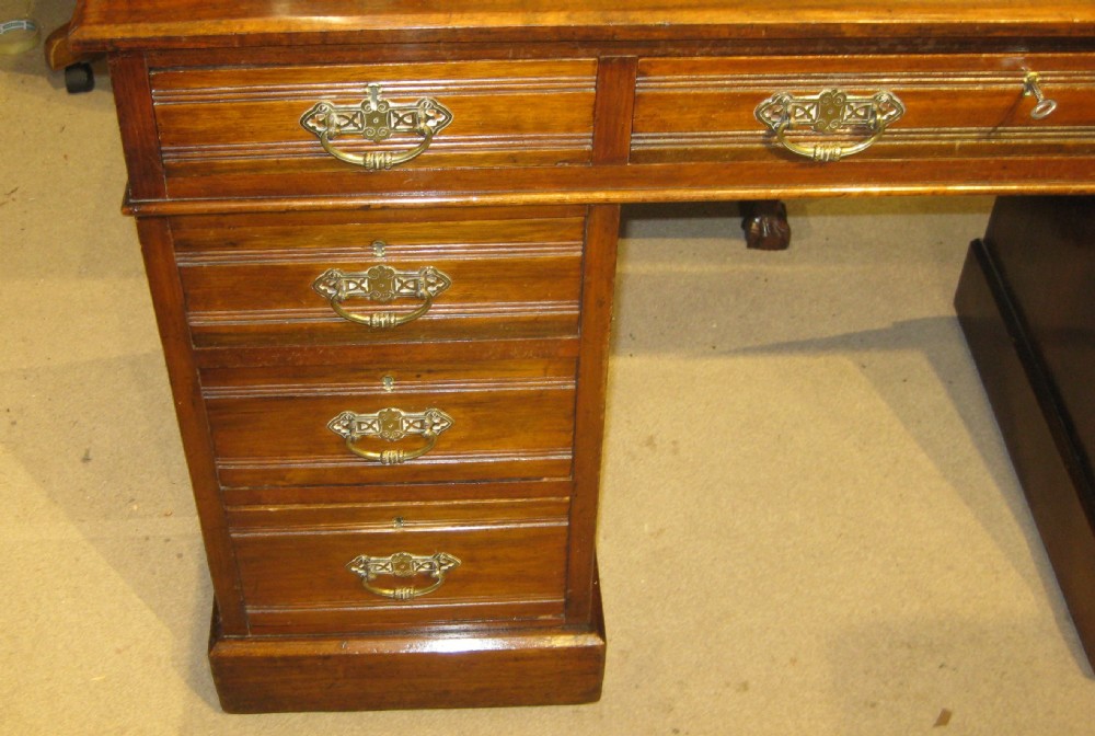 A Victorian walnut pedestal desk featuring a green leather inset top, nine drawers with ornate brass handles, and twin plinth bases. View II
