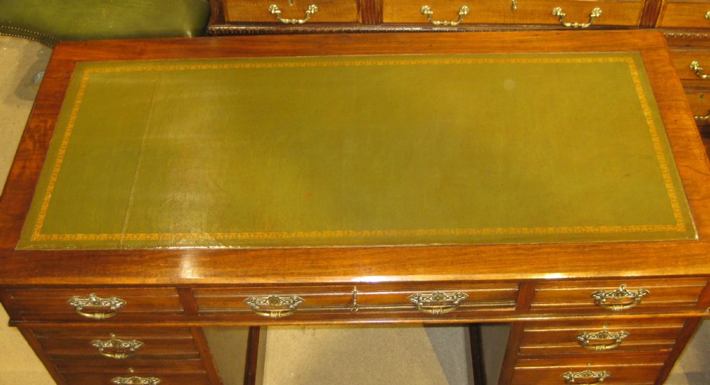 A Victorian walnut pedestal desk featuring a green leather inset top, nine drawers with ornate brass handles, and twin plinth bases. View III