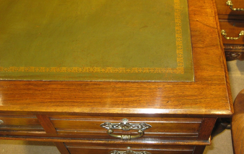 A Victorian walnut pedestal desk featuring a green leather inset top, nine drawers with ornate brass handles, and twin plinth bases. View V
