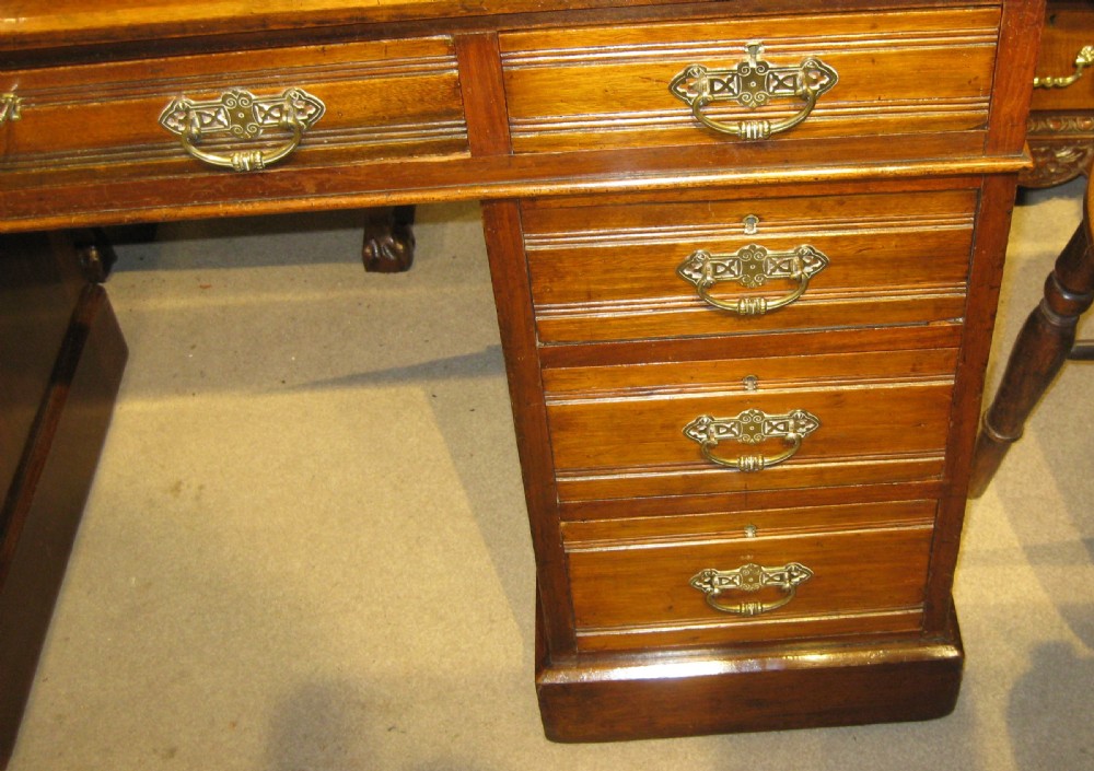 A Victorian walnut pedestal desk featuring a green leather inset top, nine drawers with ornate brass handles, and twin plinth bases. View VII