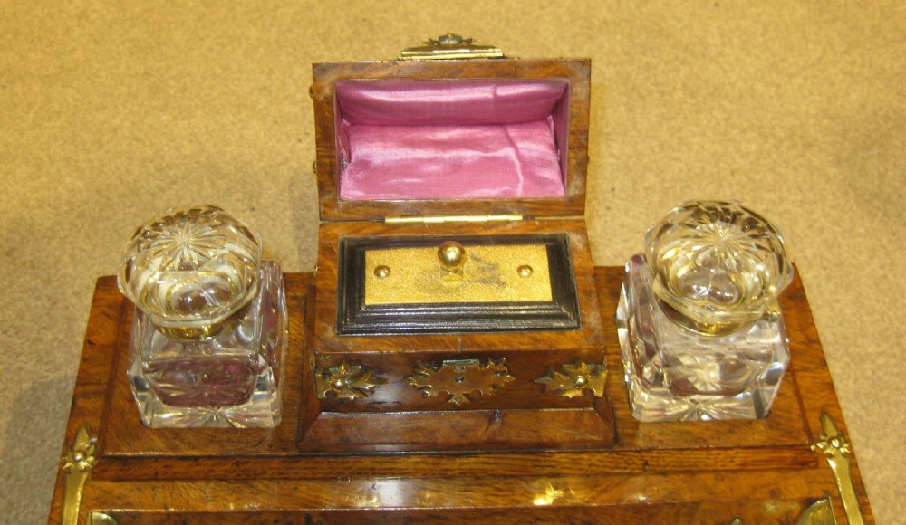 A Victorian walnut inkstand featuring polished brass Gothic strapwork, a central hinged compartment, a recessed pen tray, and two cut-glass inkwells. View V
