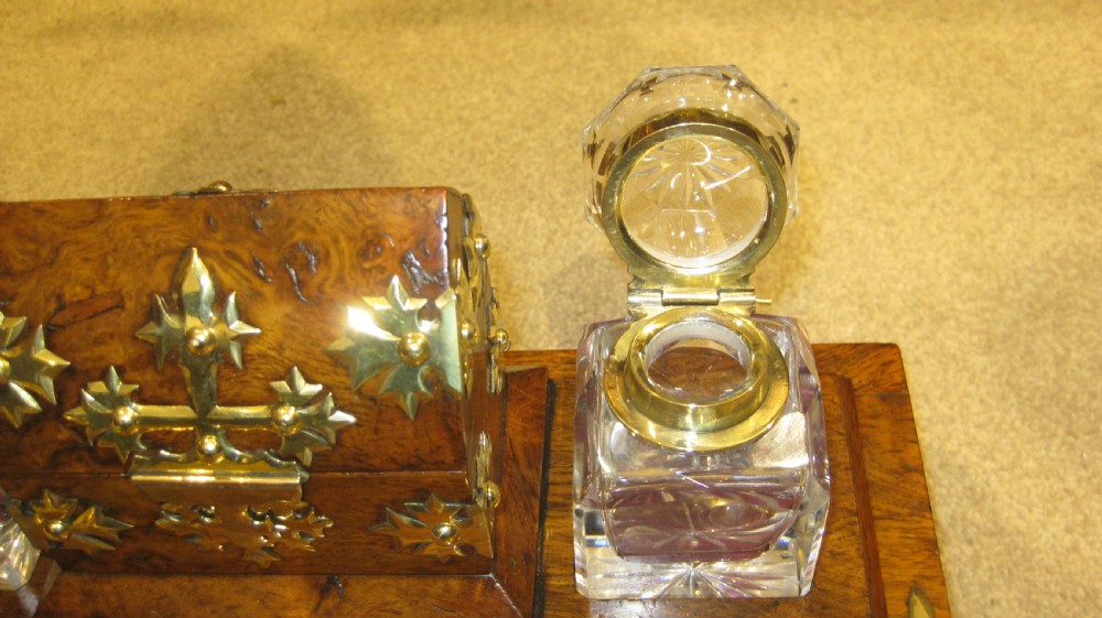 A Victorian walnut inkstand featuring polished brass Gothic strapwork, a central hinged compartment, a recessed pen tray, and two cut-glass inkwells. View VI
