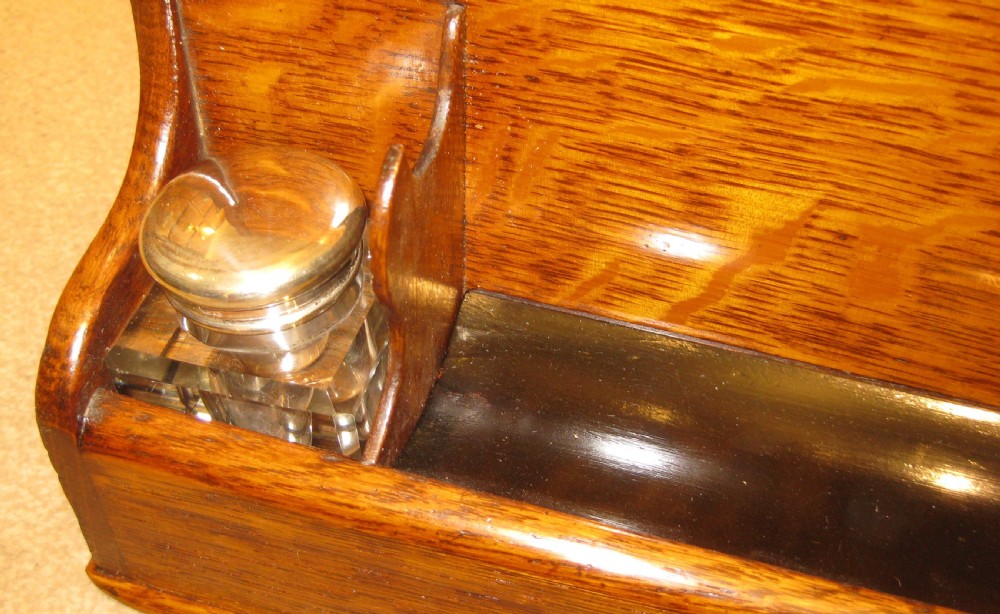 An antique golden oak stationery box featuring a curved top, brass keyhole escutcheon, lower pen recess, and two glass inkwells with metal lids. View II