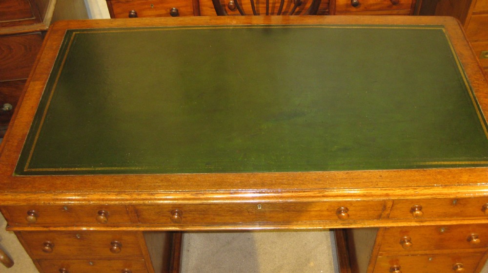 A Victorian golden oak pedestal desk featuring a green leather writing surface, nine drawers with round wooden handles, and plinth bases. View II