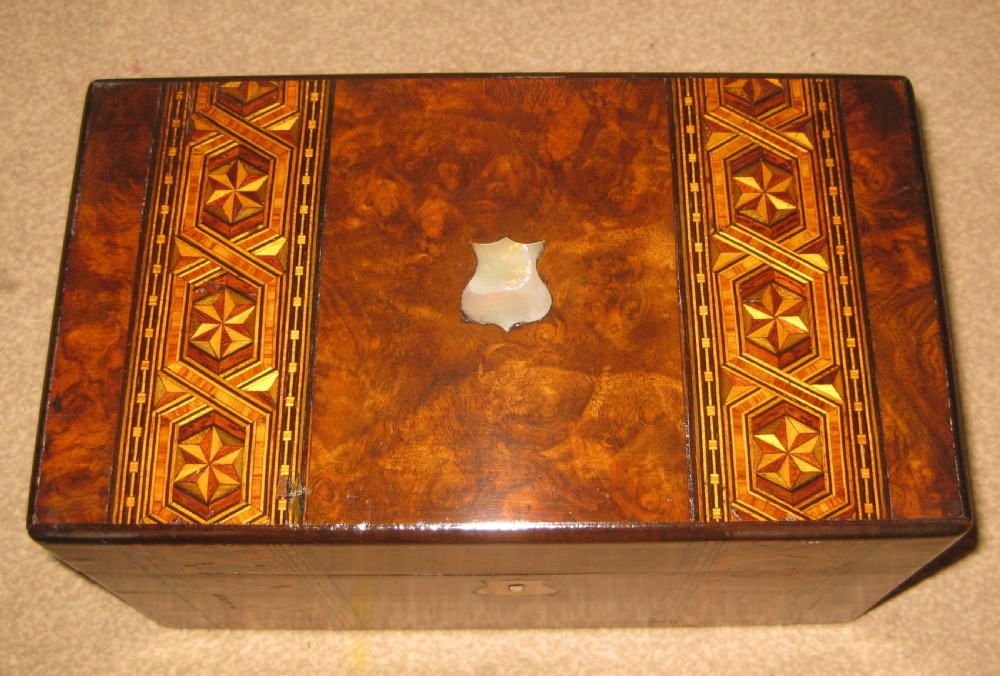 A rectangular Victorian burr walnut box with geometric inlaid wood bands across the lid and front, accented by two shield-shaped mother-of-pearl escutcheons. View IV