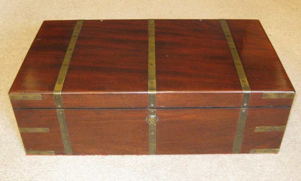 A closed rectangular dark mahogany writing box reinforced with brass straps, brass corner pieces, and a central brass keyhole.