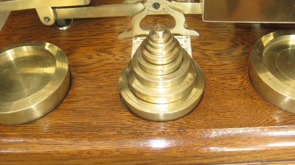 An Edwardian postal scale set featuring polished brass pans and stacked brass weights mounted on a moulded solid oak base. View II