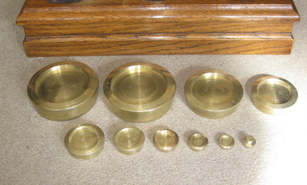 An Edwardian postal scale set featuring polished brass pans and stacked brass weights mounted on a moulded solid oak base. View V
