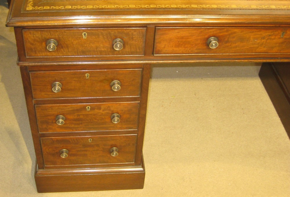 A Victorian mahogany pedestal desk featuring a tan gold-tooled leather top, nine drawers with round brass handles, and plinth bases. View II