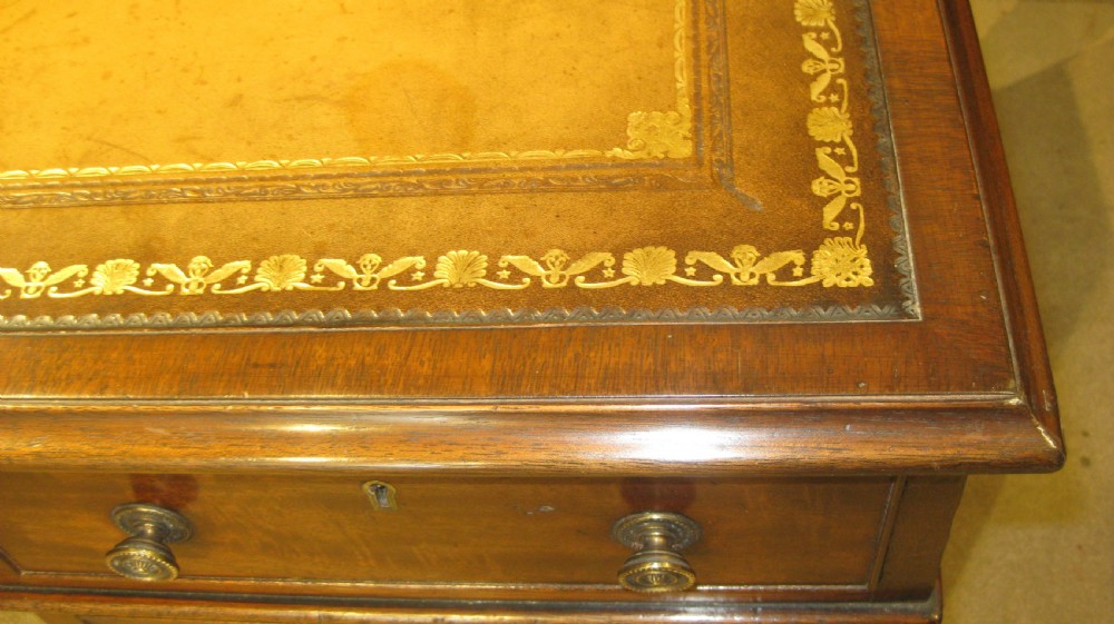 A Victorian mahogany pedestal desk featuring a tan gold-tooled leather top, nine drawers with round brass handles, and plinth bases. View V