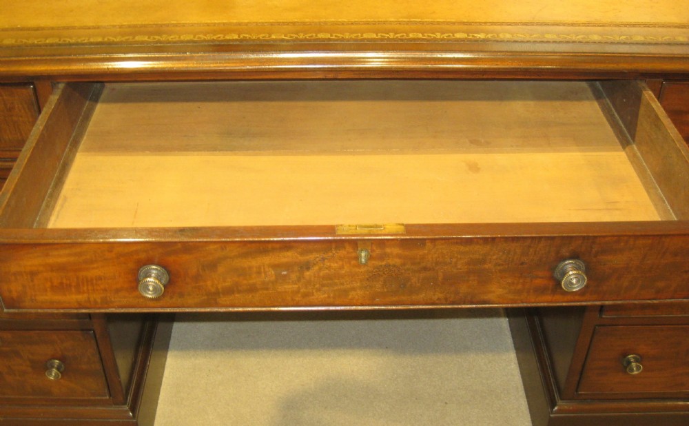 A Victorian mahogany pedestal desk featuring a tan gold-tooled leather top, nine drawers with round brass handles, and plinth bases. View VIII