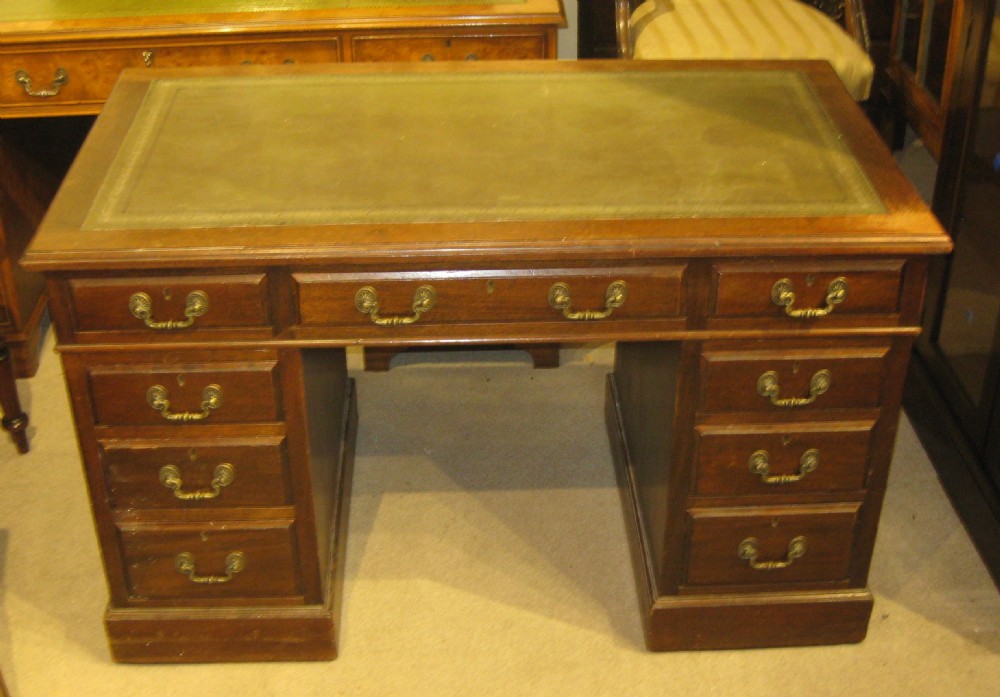 A Victorian mahogany pedestal desk featuring an olive green leather inset writing surface and nine drawers with brass handles.