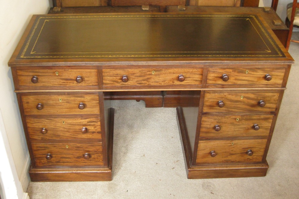 A Victorian mahogany pedestal desk featuring a dark leather writing surface with gold tooling, turned wooden knob handles, and nine storage drawers resting on twin plinth bases.