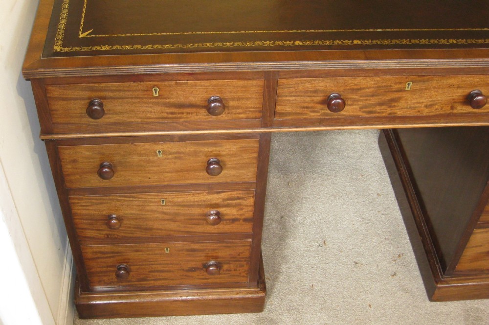 A Victorian mahogany pedestal desk featuring a dark leather writing surface with gold tooling, turned wooden knob handles, and nine storage drawers resting on twin plinth bases. View II