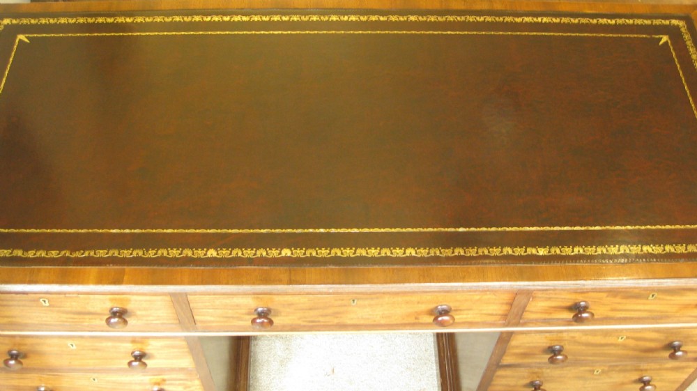 A Victorian mahogany pedestal desk featuring a dark leather writing surface with gold tooling, turned wooden knob handles, and nine storage drawers resting on twin plinth bases. View III