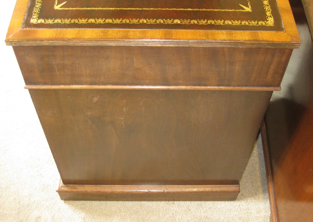 A Victorian mahogany pedestal desk featuring a dark leather writing surface with gold tooling, turned wooden knob handles, and nine storage drawers resting on twin plinth bases. View VI