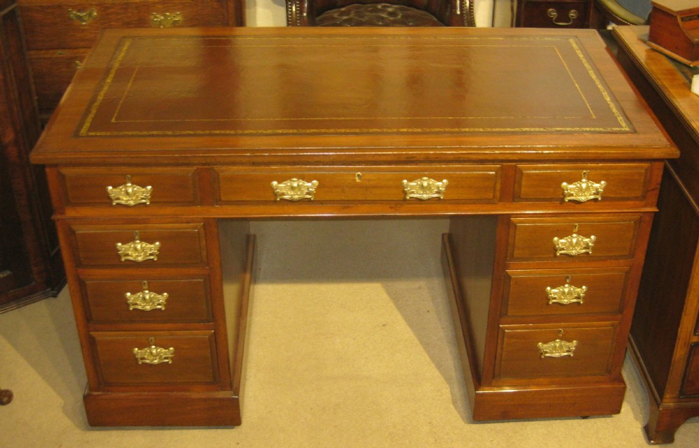 A late Victorian walnut pedestal desk featuring a gilt-tooled brown leather writing surface, nine drawers with ornate brass handles, and twin pedestals resting on plinth bases.