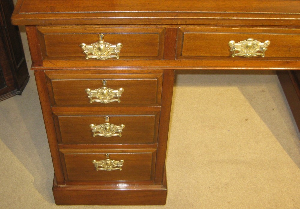 A late Victorian walnut pedestal desk featuring a gilt-tooled brown leather writing surface, nine drawers with ornate brass handles, and twin pedestals resting on plinth bases. View II