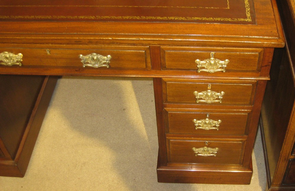 A late Victorian walnut pedestal desk featuring a gilt-tooled brown leather writing surface, nine drawers with ornate brass handles, and twin pedestals resting on plinth bases. View III