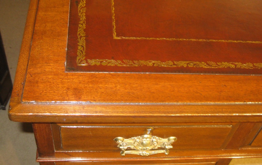 A late Victorian walnut pedestal desk featuring a gilt-tooled brown leather writing surface, nine drawers with ornate brass handles, and twin pedestals resting on plinth bases. View V