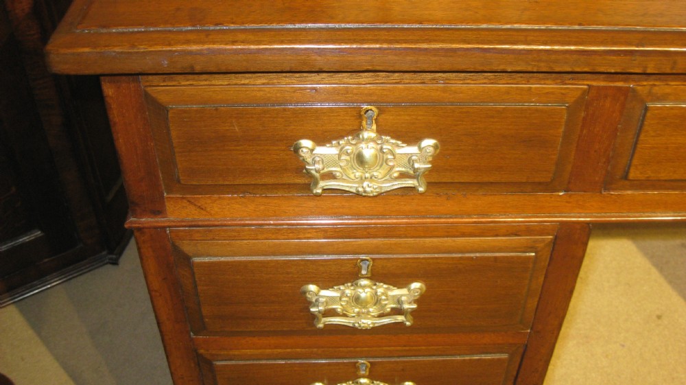 A late Victorian walnut pedestal desk featuring a gilt-tooled brown leather writing surface, nine drawers with ornate brass handles, and twin pedestals resting on plinth bases. View VI