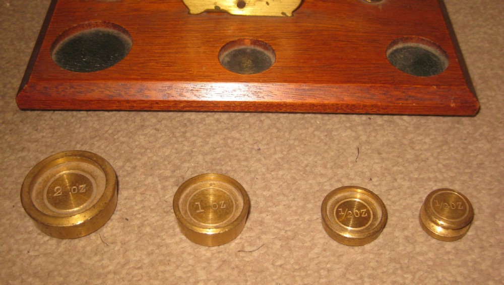 Edwardian brass balance postal scales mounted on a rectangular mahogany wooden base with recessed slots containing brass weights. View II