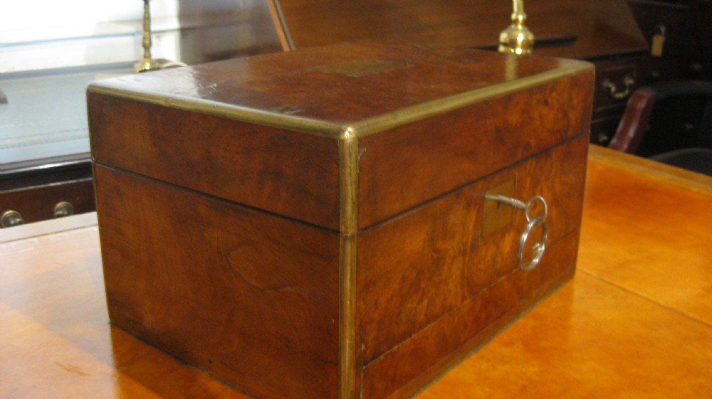 A Victorian rectangular burr walnut box featuring brass edges, a central brass cartouche, a keyhole escutcheon, and a lower drawer. View XVI