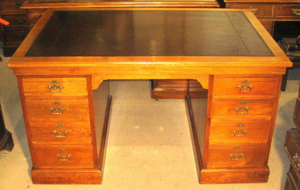 A late Victorian golden walnut pedestal desk featuring a dark leather-inlaid writing top, twin pedestals with stacked drawers, carved kneehole spandrels, and brass drop handles.